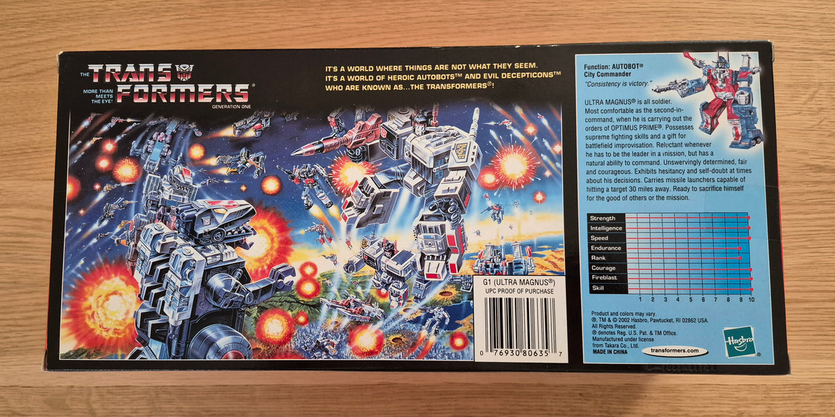 The back of a Transformers action figure box photographed flat on a light wood surface. The packaging shows colorful battle artwork, product description text, a barcode, and a small character stats chart.
