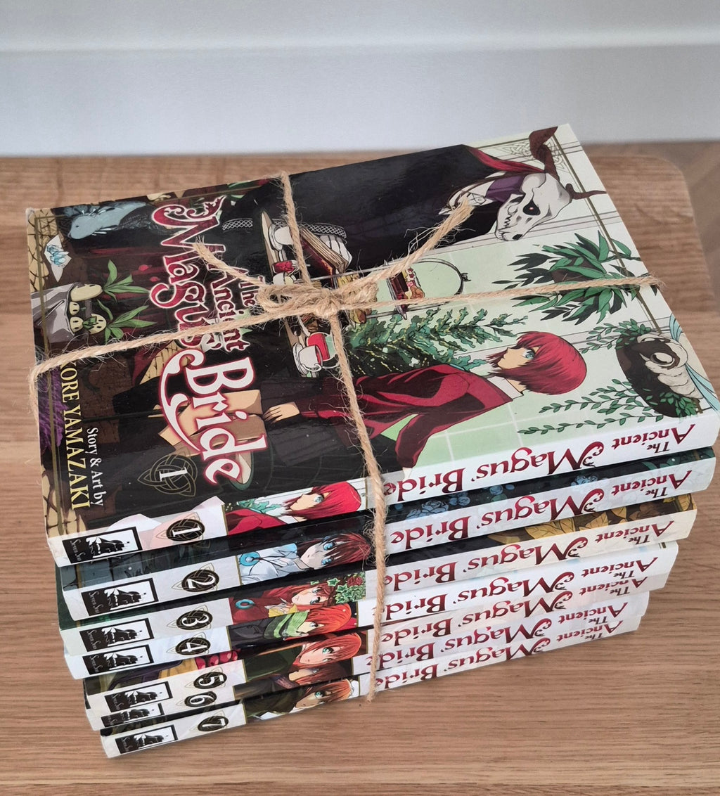 A stack of graphic novel volumes tied together with twine, placed on a wooden surface. The books are for 'The Ancient Magus Bridge' by Ore Tanjiro, published by Viz Media.