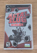 Metal Slug Anthology video game case for the Sony PSP, featuring the game's cover art with a tank and bullet holes, resting on a light wood surface.